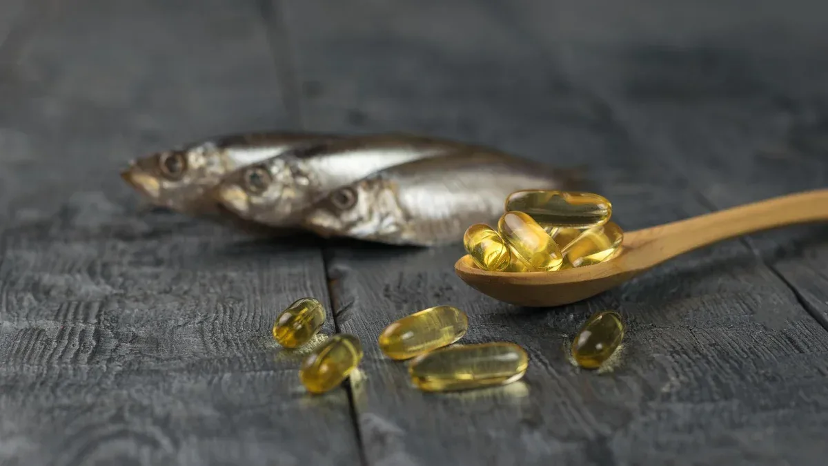 Cuillère en bois avec des capsules d'huile de poisson sur le fond de trois poissons sur une table en bois