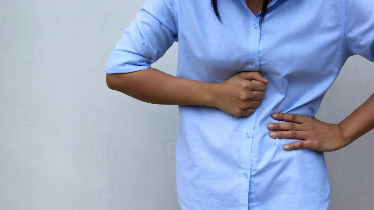 Jeune femme ressentant de la douleur avec ses maux d'estomac sur fond blanc, concept de soins de santé et de médecine