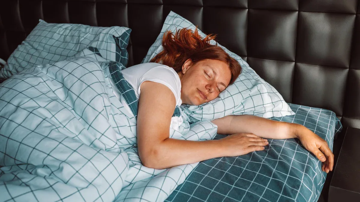 Belle jeune femme dormant le matin recouverte d'une couverture au lit dans la chambre à coucher