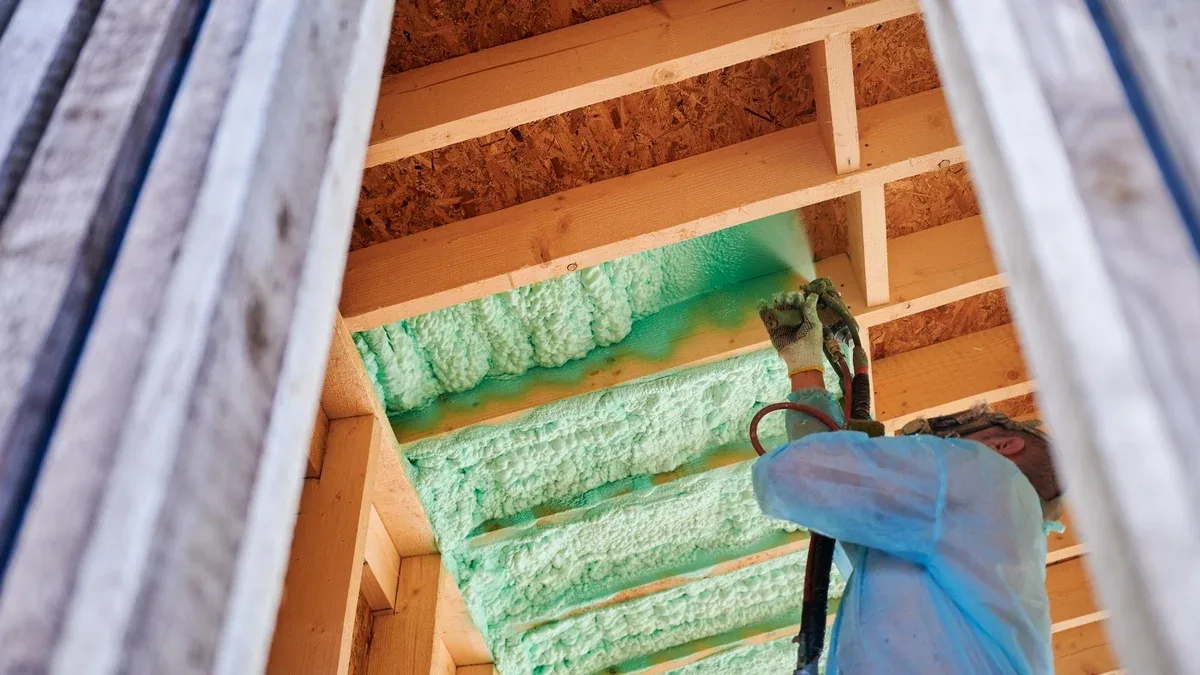Travailleur pulvérisant de la mousse de polyuréthane pour l'isolation d'une maison à charpente en bois