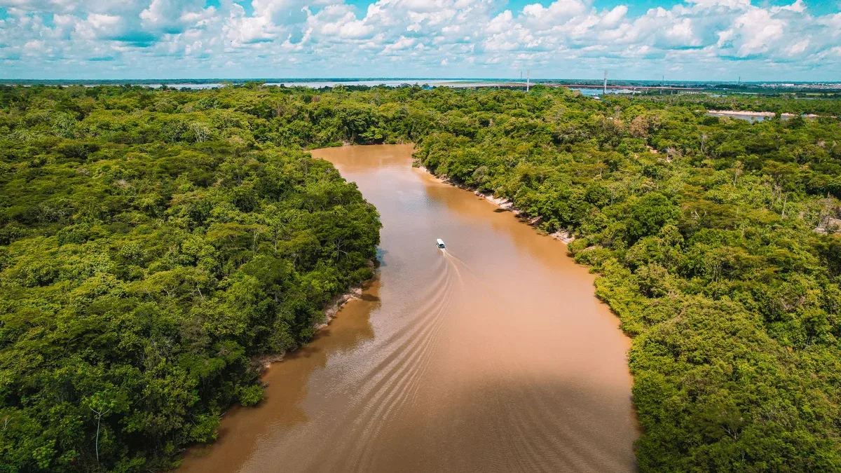 A scenic aerial shot of a boat navigating through the muddy Amazon River surrounded by lush rainforest.