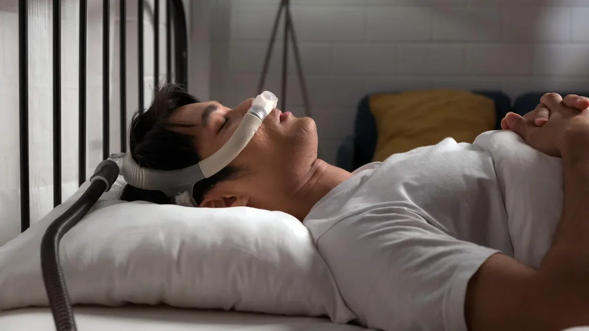 Jeune homme dormant avec un masque CPAP pour l'apnée obstructive du sommeil (AOS) et le soulagement du ronflement la nuit