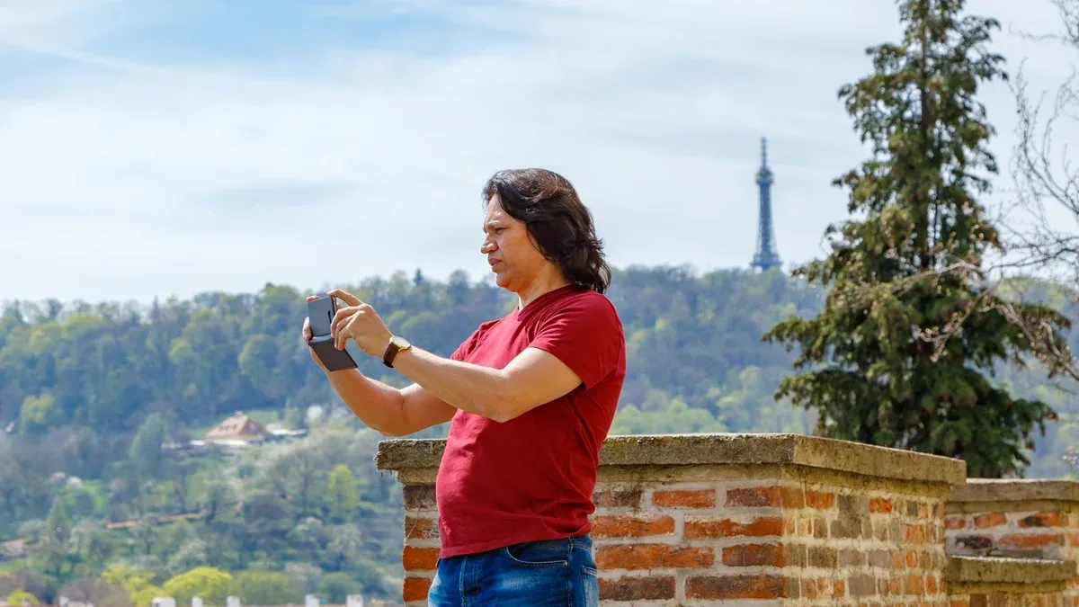 Un homme se tient sur un mur de briques et photographie le panorama de Prague