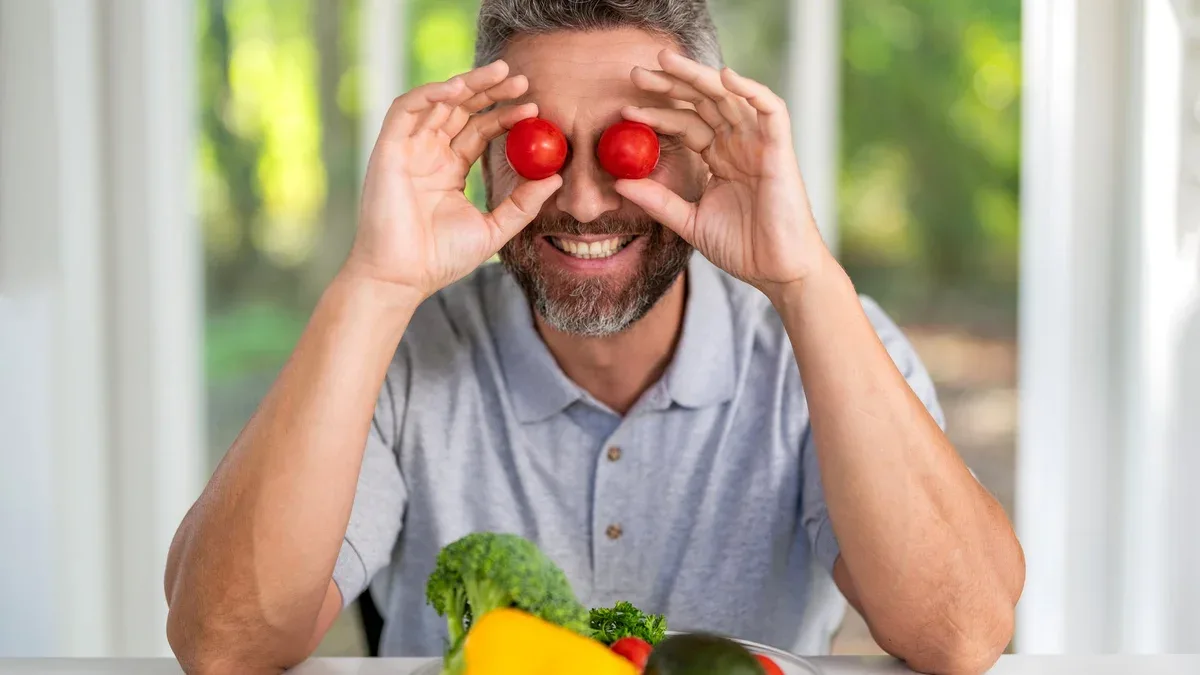 Homme mûr déjeunant dans la cuisine. Il mange des légumes bio, appréciant une alimentation saine et vitaminée. Régime alimentaire biologique